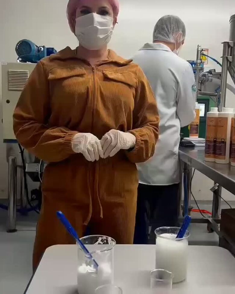 Técnica de macacão e touca no laboratório, com béqueres de formulação sobre a bancada